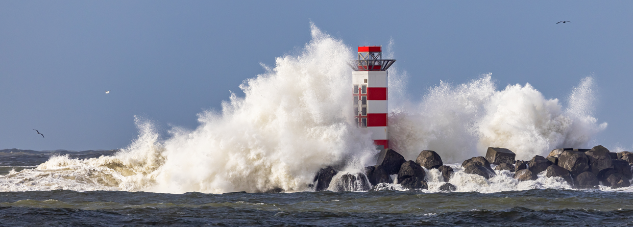 Door de harde wind ontstaan er hoge golven tegen een vuurtoren aan