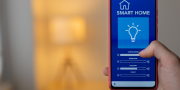 Slimme verlichting in huis: telefoon met bedieningsscherm en op de achtergrond een lamp die aan staat